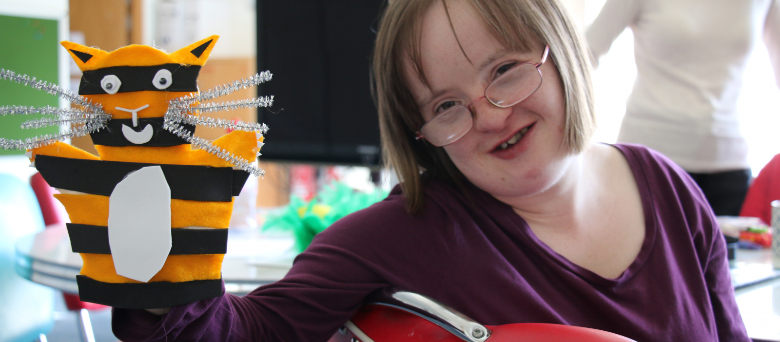 Cathers in purple jumper and glasses smiling holding orange and black cat puppet