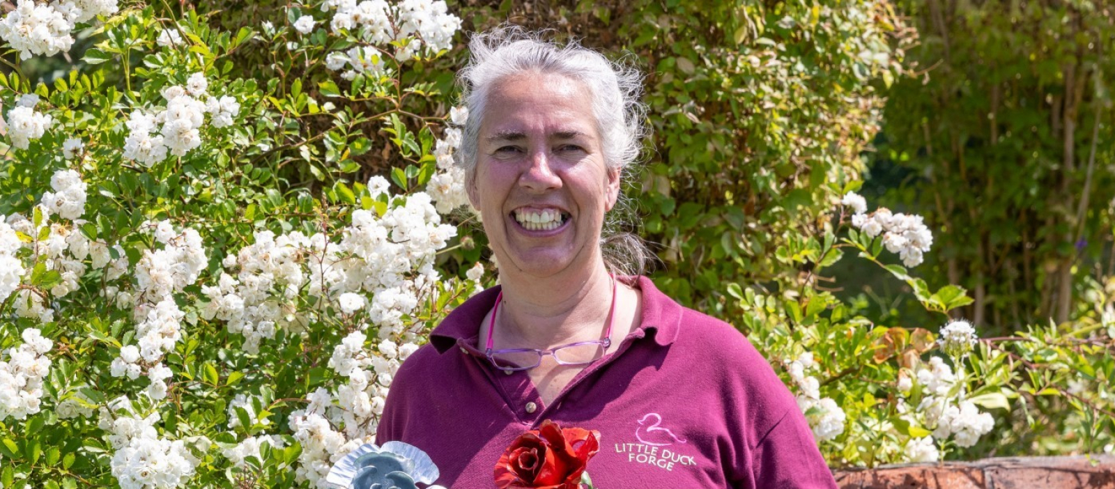 Local Blacksmith Lucille smiling and holding 2 metal roses