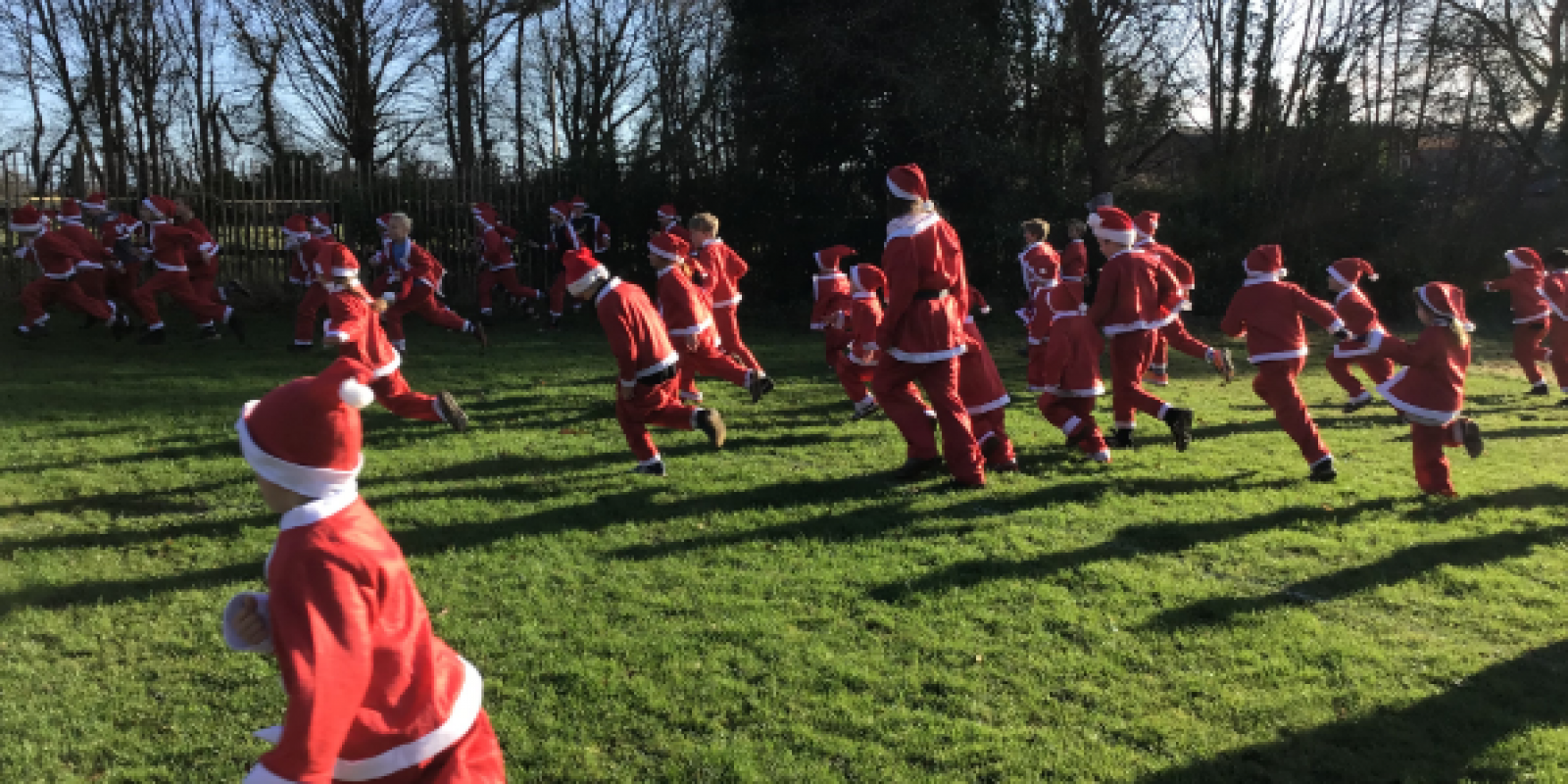 children running across a green field in red santa suits