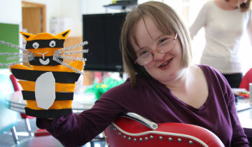 Cathers in purple jumper and glasses smiling holding orange and black cat puppet