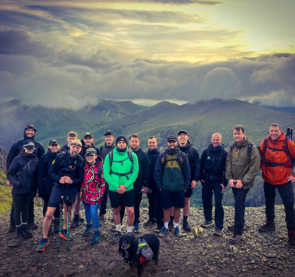 a group of people at a mountain top with clouds in the distance