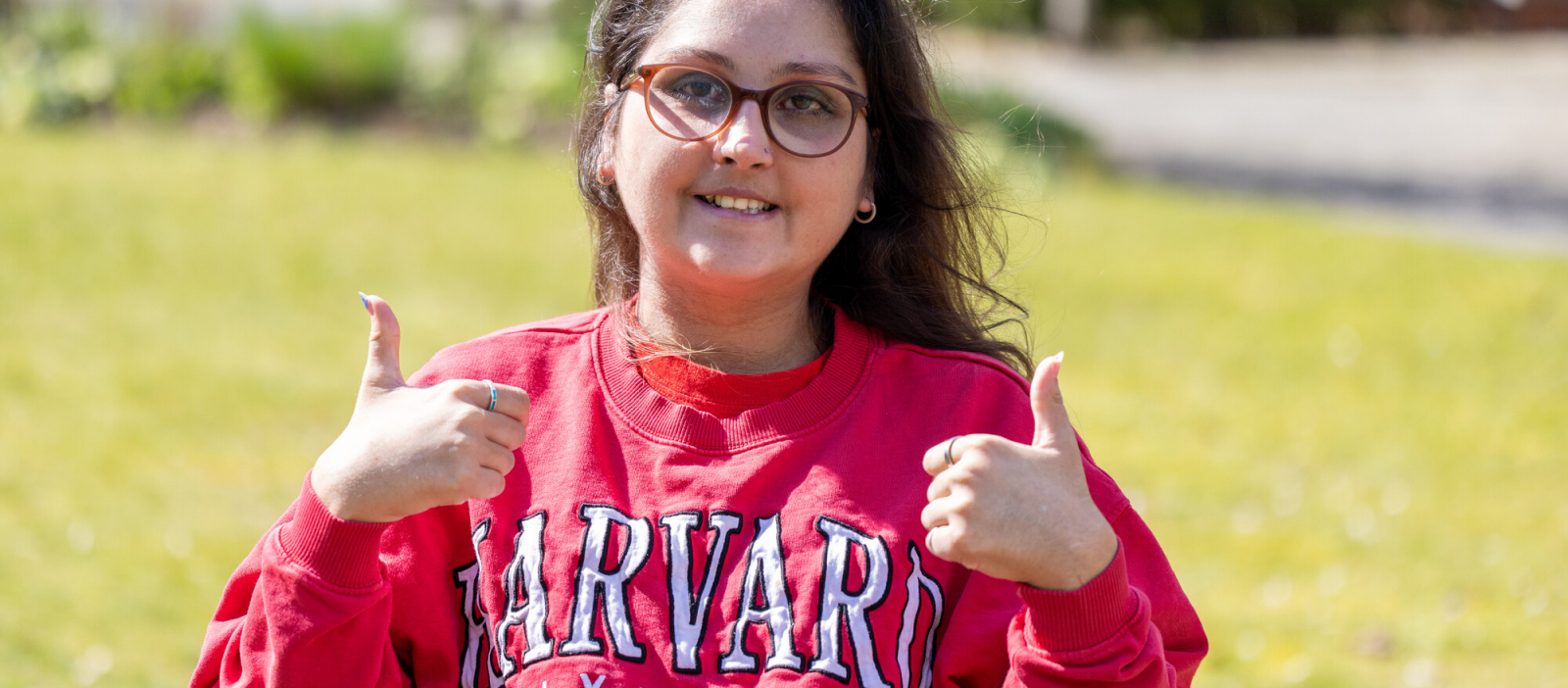 Young lady wearing glasses in red Harvard jumper with thumbs up