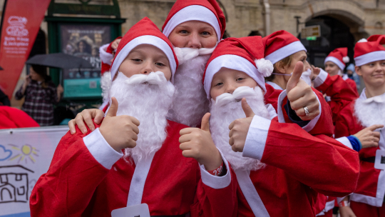 Mum and two sons in Santa suits with their thumbs up