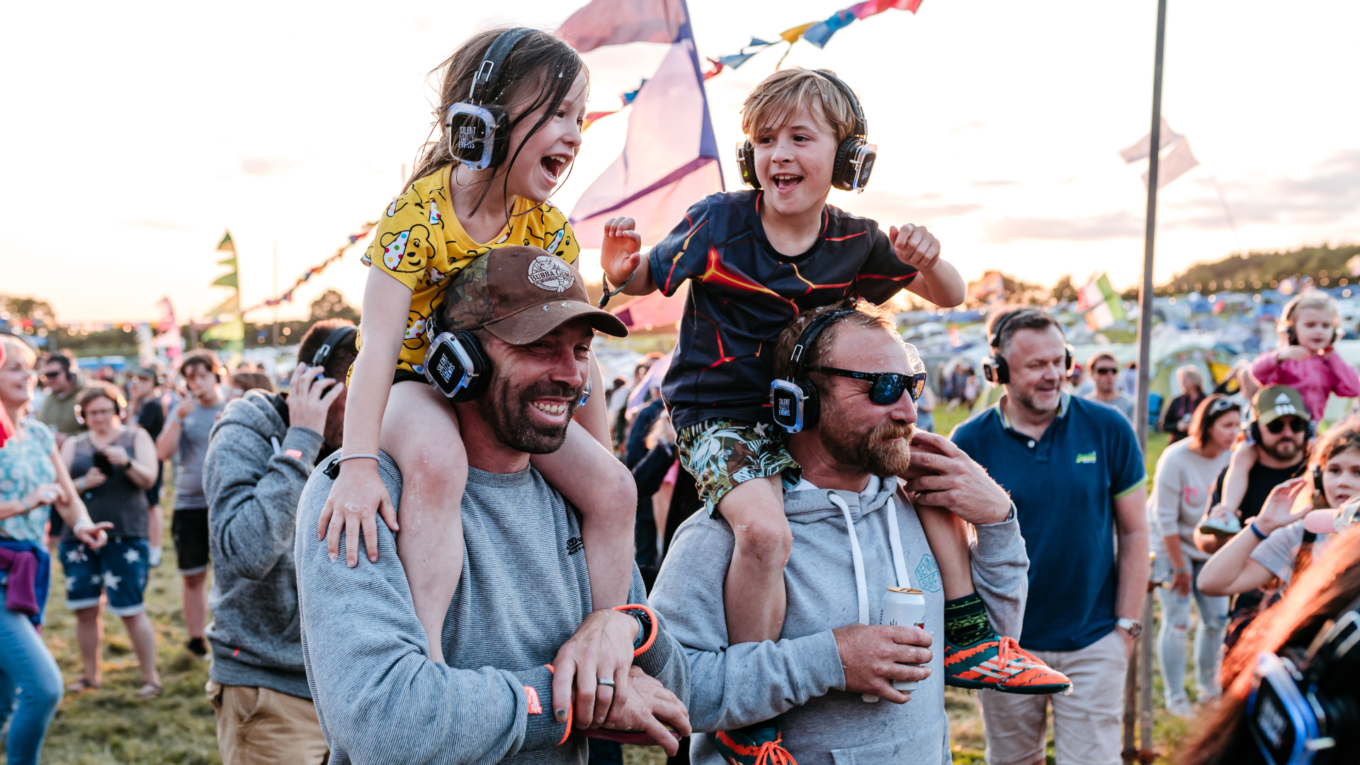 Children sat on adults' shoulders with headphones on at CarFest.jpg